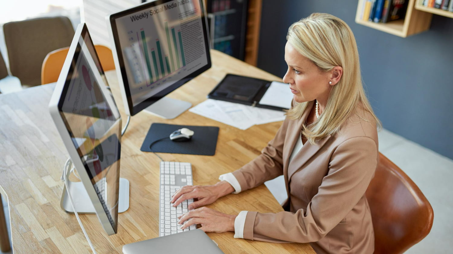 Gestora de marketing analisando gráficos de desempenho e SEO no computador em ambiente corporativo